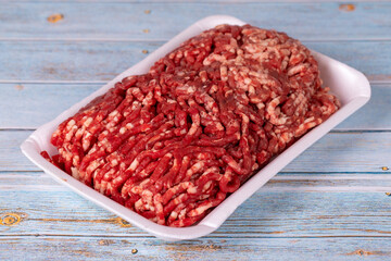 Raw ground beef in a white polystyrene tray on a wood background. Fresh ground beef on wood background.