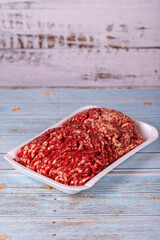 Raw ground beef in a white polystyrene tray on a wood background. Fresh ground beef on wood background.