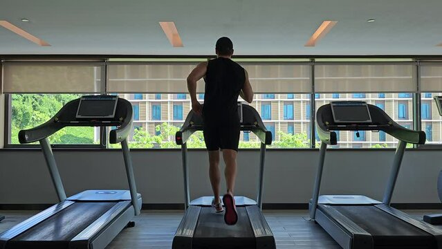 Fit Sporty Male Runner Running on Treadmill at Health Club - back view