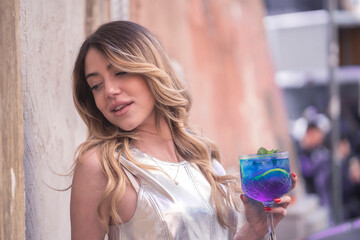 Close-up of a young woman holding a blue cocktail glass. Outdoors, one person.