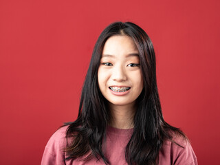Fototapeta premium A close-up portrait of a young Indonesian (Asian) woman wearing a pink shirt. Isolated with a red background