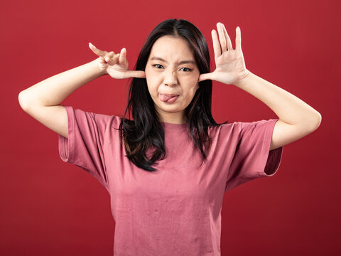 A portrait of an Asian Indonesian girl in a pink shirt making a mocking or taunting gesture with her tongue sticking out. Isolated on red background