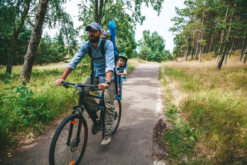 Fototapeta na wymiar Father and his little daughter cycling through the woods, the girl is sitting in the child seat
