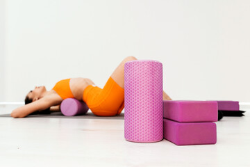 Fit athletic women in sportswear ride on a pink foam myofascial massage roller, massaging their muscles on the floor of a yoga mat in the gym. Active girls do a fitness workout in the gym. MFR