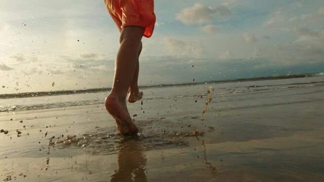 Back view of barefoot kids runs on wet sand beach in close up