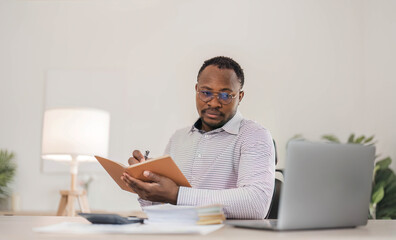 Portrait of handsome African black young business man working on laptop at office desk.