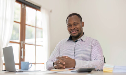 Fototapeta premium Portrait of handsome African black young business man working on laptop at office desk.
