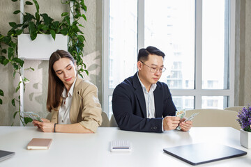 Man and woman sitting in office, holding money at hands. Gender pay gap, unequal salary concept