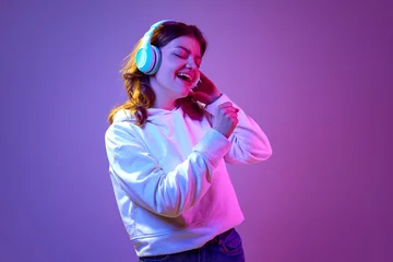 Keuken spatwand met foto Feeling good. Happy and positive young girl listening to music in headphones and singing against purple studio background in neon light. Concept of emotions, youth, lifestyle, fun, fashion © master1305