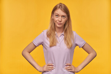 Indoor studio portrait of young ginger female with freckles looking into camera with confused facial expression isolated over yellow orange background