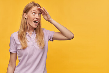 Indoor studio portrait of young ginger female with freckles looking far away isolated over yellow orange background