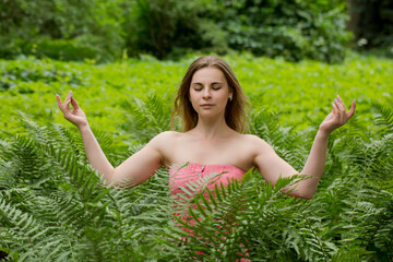 beautiful woman meditating in nature among fern leaves