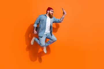 Full body profile photo of handsome guy jump hold netbook smart phone make selfie empty space isolated on orange color background