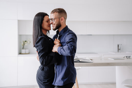 Dancing couple at home celebrating new apartment. Young adult American woman in dark suit dancing with bearded husband at home. Romance, newlyweds enjoying vacations at hotel.