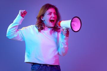 Fototapeta na wymiar Excited and emotive young man expressively shouting in megaphone against purple studio background in neon light. Sport fan support. Concept of emotions, youth, lifestyle, propaganda, news, event