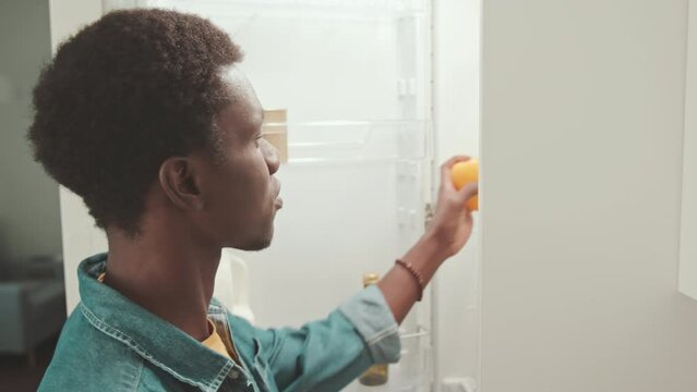 Young Black man putting fresh groceries in fridge at home
