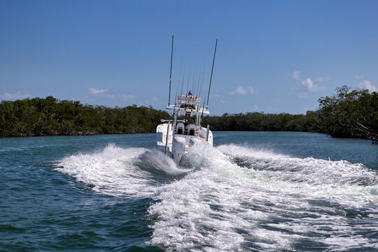 Center console fishing boat speeding away near mangrove trees.