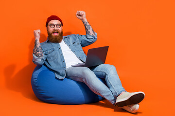 Full length photo of delighted young freelancer working netbook win start up project sit bean chair isolated shine color background