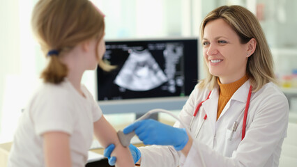 Doctor traumatologist making ultrasound examination of elbows of little girl in clinic. Diagnosis...