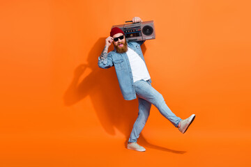 Full length photo of confident cool man wear jeans shirt dancing listening boom box isolated orange color background