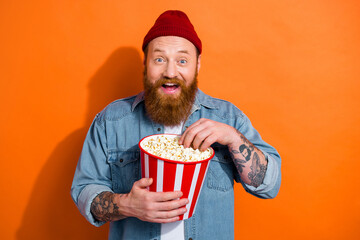 Photo of excited cheerful man wear jeans shirt watching movie eating popcorn isolated orange color background