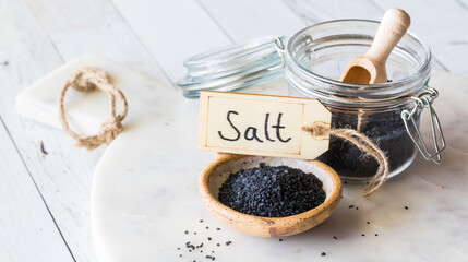 A small bowl of black Hawaiian rock salt on a white marble slab.