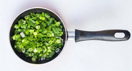Chopped spring onions or chives isolated in frying pan on white background, top view