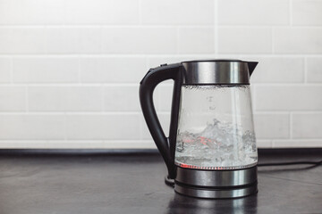 Water Boiling in Modern Transparent Electric Kettle on Black Table and White Tiles on Wall Kitchen
