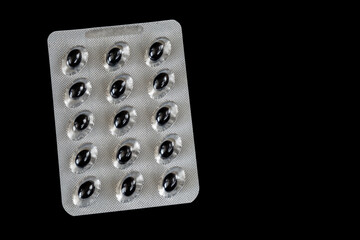 Black oval tablets in a blister pack isolated on a black background