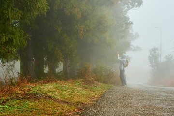 Young man in the foggy forest doing photography while hiking