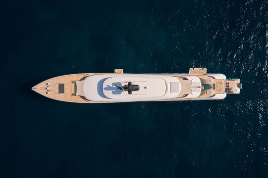 Innovative white big yacht anchored in the morning sun top view. Mega yacht on a dark background aerial view.