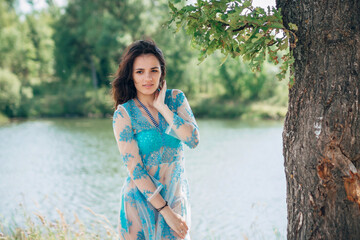 young girl with a sexy body in a swimsuit and tunic smiles on beach by lake in summer