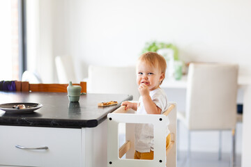 Young australian baby eating vegemite toast at kitchen bench standing on Montessori learning tower
