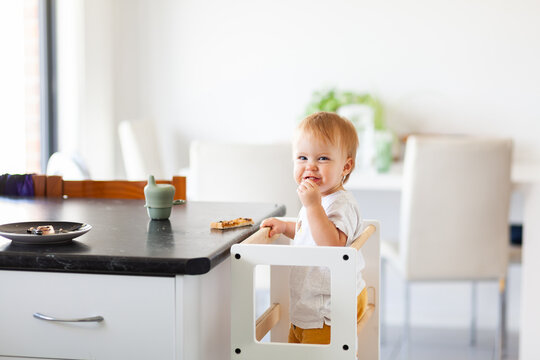 Young australian baby eating vegemite toast at kitchen bench standing on Montessori learning tower