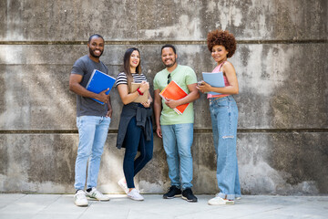 Diverse group of college students. Happy multiethnic young friends in casual clothes with ,class textbooks posing standing near a wall while looking at camera.