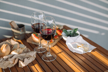 Glasses of red wine with tasty snacks on table in beautiful golden hour. Romantic dinner for a...
