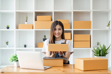 Young business woman working online e-commerce shopping at her shop. Young woman seller prepare parcel box of product for deliver to customer. Online selling