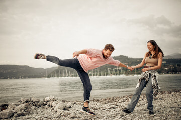 The cute hipster couple having fun at the Italian lake Garda coast jumping and smiling widely