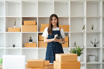 Fototapeta na wymiar Startup SME small business entrepreneur of freelance Asian woman using tablet and box to receive and review orders online to prepare to pack sell to customers, online sme business ideas