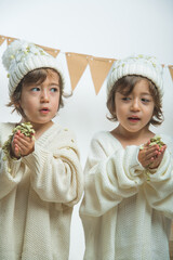 Photo session with twins dressed in white sweaters and wool caps posing and playing with confetti.