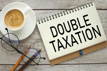 Double taxation symbol.Finance and business concept. On a wooden background, a notepad with text with a cup of coffee and glasses