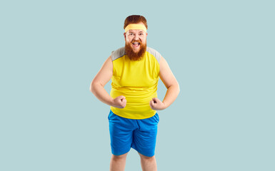 Funny chubby sportsman flexing arms and showing weak muscles. Happy excited fat bearded man in...
