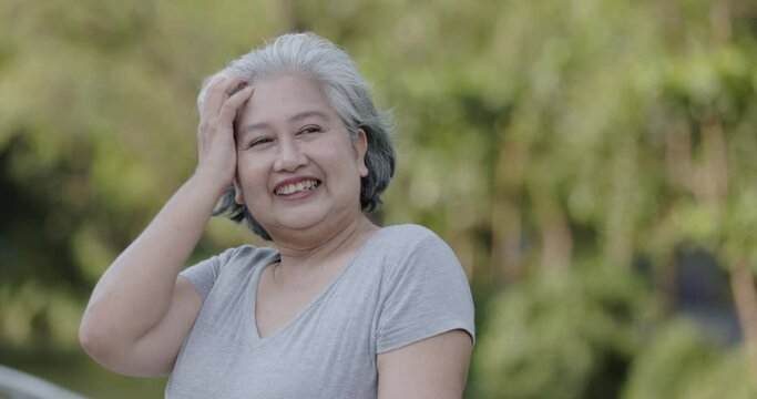 Gray-haired Asian elderly woman standing happily smiling in the park. Close Up Face Of An Old Woman Expressing Positive Emotions. health care of the elderly. Concept International Day of Older Persons