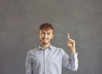 Casual red-haired man having bright idea pointing finger up studio shot portrait. Excited young...