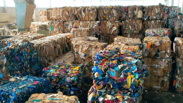 Multiple stacks of cubes of compressed paper and plastic garbage at waste sorting plant. Slow motion