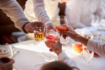 Cheers! Group of people cheering with glass with alcohol with home interior in the background. Restaurant Chilling Out Classy Lifestyle Reserved Concept. Friends clinking glasses above dinner table. 