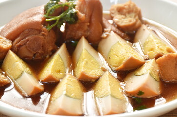 boiled half cut egg with tofu in herb brown soup and pork leg on plate 