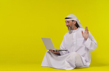 Concept online communication. Muslim person sitting on floor greets someone with their palm raised while holding a laptop in their hand. Copy space allows for easy customization and versatility and