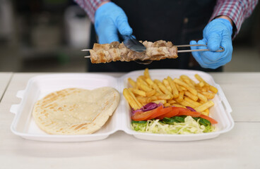 Cook preparing traditional Greek kalamaki dish in a restaurant kitchen. Chef put grilled pork meat...