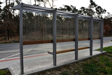Fototapeta premium city bus stop. glass shelter with integrated wooden bench. only the roof and the back wall. on the street by the sidewalk in the city. elegant arch, station, platform, lawn, grass, tactile